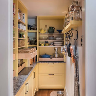 Mittelgroße Country Küche in L-Form mit Vorratsschrank, Unterbauwaschbecken, Schrankfronten im Shaker-Stil, gelben Schränken, Arbeitsplatte aus Holz, Küchenrückwand in Braun, Rückwand aus Steinfliesen, Küchengeräten aus Edelstahl, braunem Holzboden, Kücheninsel und braunem Boden in Boston