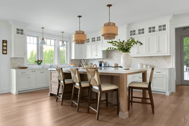 Example of a large transitional light wood floor kitchen design in New York with an undermount sink, shaker cabinets, white cabinets, quartz countertops, white backsplash, paneled appliances and an island