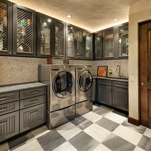 Diseño de cuarto de lavado en L, mediterráneo, grande, con fregadero bajoencimera, armarios tipo vitrina, puertas de armario grises, encimera de mármol, paredes beige, suelo de baldosas de porcelana y lavadora y secadora juntas