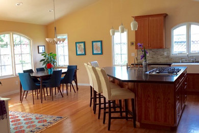 Mid-sized transitional l-shaped medium tone wood floor open concept kitchen photo in San Francisco with a farmhouse sink, shaker cabinets, medium tone wood cabinets, quartz countertops, multicolored backsplash, glass tile backsplash, stainless steel appliances and an island