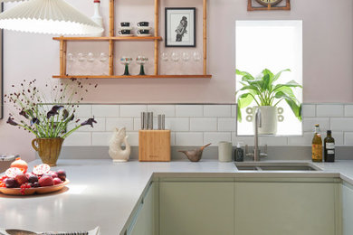 Eclectic u-shaped kitchen in London with a double-bowl sink, flat-panel cabinets, green cabinets, white splashback, subway tile splashback, a peninsula, brown floor and grey benchtop.
