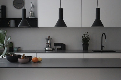Offene, Große Moderne Küche in L-Form mit Unterbauwaschbecken, flächenbündigen Schrankfronten, weißen Schränken, Mineralwerkstoff-Arbeitsplatte, schwarzen Elektrogeräten, hellem Holzboden, Kücheninsel, braunem Boden und schwarzer Arbeitsplatte in Köln