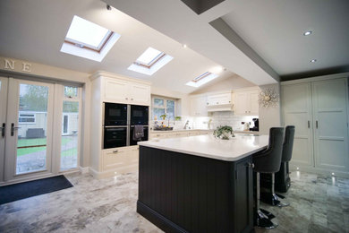 This is an example of a large traditional open plan kitchen in West Midlands with shaker cabinets, quartz worktops, white splashback, metro tiled splashback, an island and white worktops.