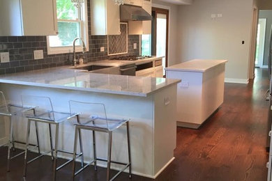 Large transitional u-shaped open plan kitchen in Chicago with a farmhouse sink, shaker cabinets, white cabinets, quartzite benchtops, grey splashback, subway tile splashback, stainless steel appliances, medium hardwood floors, with island and brown floor.