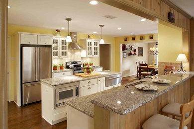 Design ideas for a mid-sized traditional galley kitchen in Dallas with glass-front cabinets, white cabinets, granite benchtops, beige splashback, stone tile splashback, stainless steel appliances, dark hardwood floors, with island and brown floor.