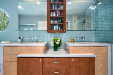 Large beach style ensuite bathroom in Miami with flat-panel cabinets, medium wood cabinets, a built-in bath, a corner shower, a one-piece toilet, blue tiles, blue walls, a vessel sink, grey floors, a hinged door, grey worktops, double sinks and a built in vanity unit.
