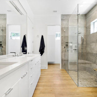 Example of a trendy master gray tile light wood floor and beige floor walk-in shower design in Orlando with flat-panel cabinets, white cabinets, white walls, an undermount sink and a hinged shower door
