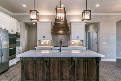 Mid-sized arts and crafts l-shaped medium tone wood floor and brown floor kitchen photo in Other with a farmhouse sink, shaker cabinets, white cabinets, granite countertops, multicolored backsplash, mosaic tile backsplash, white appliances and an island