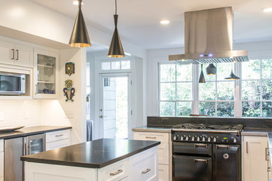 Inspiration for a modern separate kitchen in Raleigh with shaker cabinets, white cabinets, stainless steel benchtops, white splashback, subway tile splashback, stainless steel appliances, light hardwood floors, with island, multi-coloured floor and black benchtop.