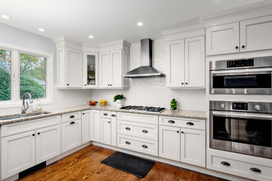 Inspiration for a mid-sized transitional l-shaped dark wood floor and brown floor kitchen remodel in Bridgeport with an undermount sink, recessed-panel cabinets, white cabinets, granite countertops, white backsplash, subway tile backsplash, stainless steel appliances and no island