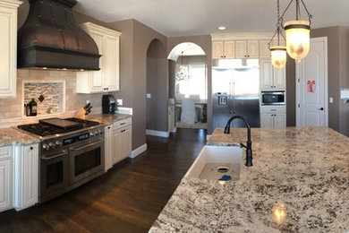 Inspiration for a large transitional u-shaped dark wood floor and brown floor open concept kitchen remodel in Denver with a farmhouse sink, raised-panel cabinets, white cabinets, granite countertops, beige backsplash, stone tile backsplash, stainless steel appliances, an island and gray countertops