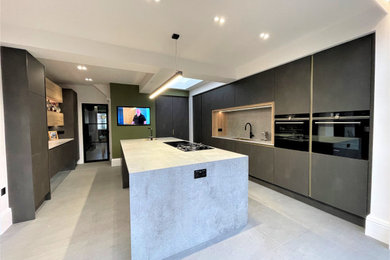 Large contemporary grey and black single-wall kitchen in Other with a single-bowl sink, flat-panel cabinets, medium wood cabinets, composite countertops, grey splashback, black appliances, ceramic flooring, an island, grey floors, grey worktops and a feature wall.