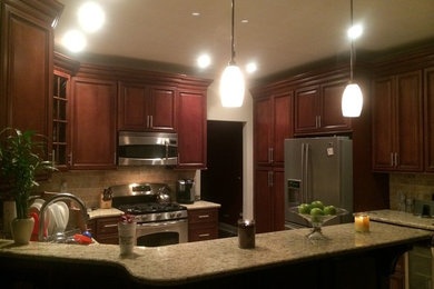 Eat-in kitchen - mid-sized traditional u-shaped porcelain tile eat-in kitchen idea in New York with an undermount sink, raised-panel cabinets, dark wood cabinets, granite countertops, beige backsplash, stone tile backsplash, stainless steel appliances and a peninsula