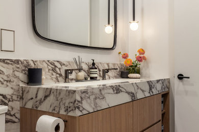 Example of a small trendy master porcelain tile, gray floor and double-sink alcove shower design in Toronto with flat-panel cabinets, light wood cabinets, a one-piece toilet, white walls, a trough sink, a hinged shower door and a built-in vanity