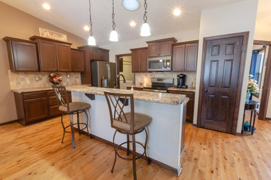 Elegant medium tone wood floor eat-in kitchen photo in Milwaukee with dark wood cabinets, laminate countertops, brown backsplash, stone tile backsplash, stainless steel appliances and an island