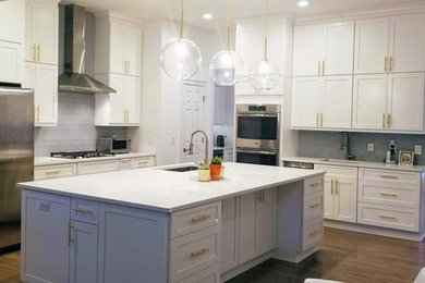 Inspiration for a large transitional l-shaped medium tone wood floor and brown floor open concept kitchen remodel in Miami with shaker cabinets, white cabinets, an island, white countertops, an undermount sink, glass tile backsplash, stainless steel appliances, quartz countertops and gray backsplash