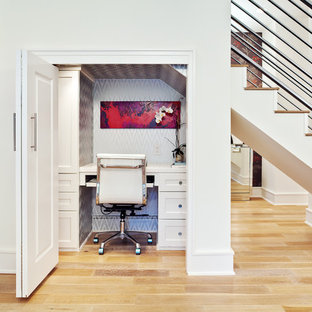 Inredning av ett klassiskt litet hemmabibliotek, med vita väggar, ljust trägolv, ett inbyggt skrivbord och beiget golv