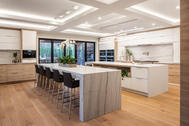 Design ideas for a large contemporary single-wall open plan kitchen in Vancouver with a farmhouse sink, flat-panel cabinets, light wood cabinets, quartzite benchtops, white splashback, marble splashback, stainless steel appliances, medium hardwood floors, multiple islands, brown floor, white benchtop and coffered.