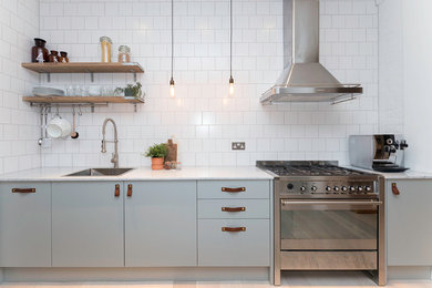 Inspiration for a scandinavian kitchen in London with a drop-in sink, flat-panel cabinets, blue cabinets, white splashback, subway tile splashback, stainless steel appliances and light hardwood floors.