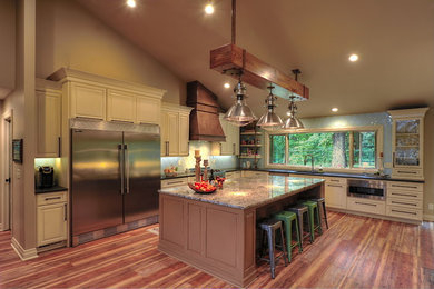 Mid-sized country l-shaped open plan kitchen in Omaha with an undermount sink, raised-panel cabinets, beige cabinets, granite benchtops, blue splashback, glass tile splashback, stainless steel appliances, vinyl floors, with island, brown floor and blue benchtop.