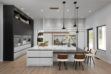 Example of a trendy l-shaped medium tone wood floor and brown floor kitchen design in Oklahoma City with flat-panel cabinets, black cabinets, quartz countertops, white backsplash, quartz backsplash, paneled appliances, an island, white countertops and an undermount sink