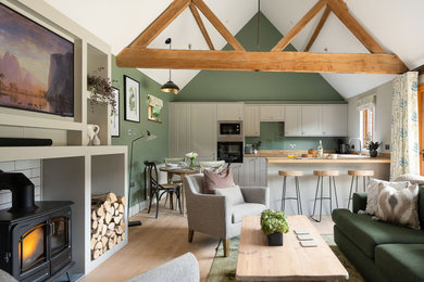 This is an example of a small country open plan living room in Hampshire with green walls, light hardwood flooring, a wood burning stove, a wooden fireplace surround, a built-in media unit and brown floors.