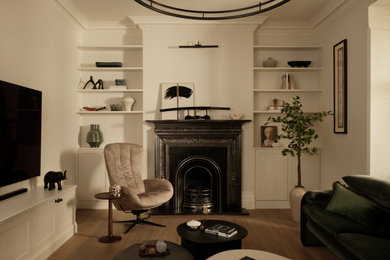 This is an example of a medium sized traditional formal and cream and black enclosed living room in London with beige walls, medium hardwood flooring, a standard fireplace, a stone fireplace surround, brown floors and a chimney breast.