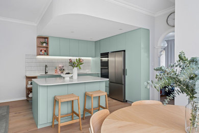 Contemporary l-shaped open plan kitchen in Perth with an undermount sink, flat-panel cabinets, turquoise cabinets, white splashback, mosaic tile splashback, stainless steel appliances, light hardwood floors, with island, beige floor and white benchtop.