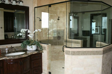 This is an example of a large eclectic master wet room bathroom in San Diego with raised-panel cabinets, dark wood cabinets, brown tile, gray tile, glass tile, beige walls, travertine floors, an undermount sink, granite benchtops, beige floor and a hinged shower door.