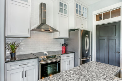 Photo of a mid-sized transitional l-shaped eat-in kitchen in Wichita with a farmhouse sink, white cabinets, granite benchtops, white splashback, ceramic splashback, stainless steel appliances, dark hardwood floors, with island and brown floor.