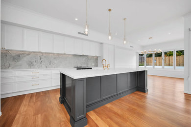 Design ideas for an expansive traditional l-shaped kitchen in Brisbane with a farmhouse sink, shaker cabinets, black cabinets, limestone benchtops, grey splashback, limestone splashback, black appliances, medium hardwood floors, with island, brown floor, grey benchtop and recessed.