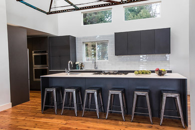 Example of a large minimalist galley medium tone wood floor and brown floor open concept kitchen design in Salt Lake City with a single-bowl sink, flat-panel cabinets, gray cabinets, solid surface countertops, white backsplash, glass tile backsplash, stainless steel appliances and an island