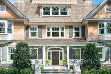 Photo of an expansive beach style three-storey grey house exterior in New York with wood siding, a hip roof and a shingle roof.