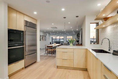 Inspiration for a large contemporary l-shaped light wood floor and beige floor open concept kitchen remodel in Vancouver with an undermount sink, flat-panel cabinets, light wood cabinets, quartz countertops, white backsplash, ceramic backsplash, black appliances, a peninsula and white countertops