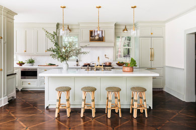 Example of a large classic single-wall dark wood floor and brown floor eat-in kitchen design in New York with a farmhouse sink, recessed-panel cabinets, beige cabinets, marble countertops, white backsplash, marble backsplash, stainless steel appliances, an island and white countertops