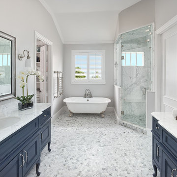 Crisp Master Bathroom with Navy Blue Freestanding Vanities and Claw-foot Tub