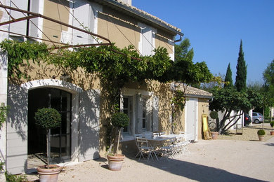 Cette image montre une façade de maison beige rustique en stuc de taille moyenne et à un étage avec un toit à deux pans et un toit en tuile.
