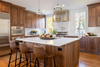 Example of a large transitional l-shaped medium tone wood floor kitchen design in Boston with an undermount sink, shaker cabinets, medium tone wood cabinets, quartz countertops, white backsplash, ceramic backsplash, stainless steel appliances, an island and white countertops