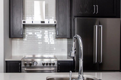 Eat-in kitchen - small modern galley dark wood floor and brown floor eat-in kitchen idea in New York with an undermount sink, shaker cabinets, black cabinets, quartz countertops, white backsplash, ceramic backsplash, stainless steel appliances, an island and black countertops