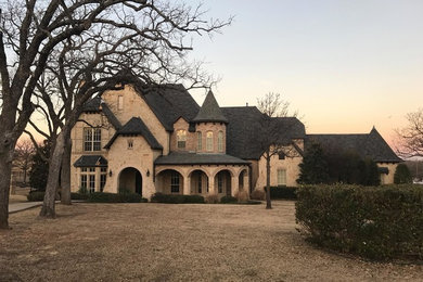 Example of a large ornate beige two-story stone house exterior design in Dallas with a hip roof and a shingle roof