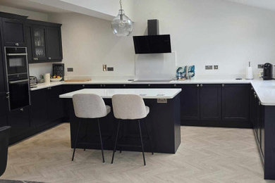 This is an example of a large contemporary u-shaped kitchen/diner in West Midlands with an integrated sink, shaker cabinets, blue cabinets, quartz worktops, white splashback, marble splashback, black appliances, light hardwood flooring, an island, grey floors, blue worktops and a coffered ceiling.
