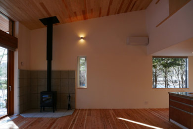 他の地域にあるおしゃれなリビング (白い壁、淡色無垢フローリング、薪ストーブ、石材の暖炉まわり、据え置き型テレビ、茶色い床、板張り天井) の写真