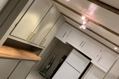 Example of a mid-sized arts and crafts galley vinyl floor, white floor and wall paneling utility room design in San Francisco with a drop-in sink, shaker cabinets, white cabinets, wood countertops, gray backsplash, ceramic backsplash, gray walls, a side-by-side washer/dryer and brown countertops