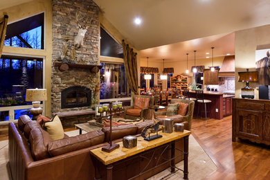 This is an example of a mid-sized country formal open concept living room in Denver with beige walls, medium hardwood floors, a standard fireplace, a stone fireplace surround, no tv and brown floor.