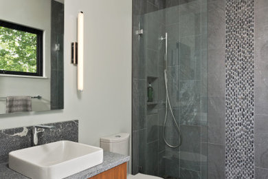 Medium sized modern family bathroom in New York with flat-panel cabinets, medium wood cabinets, a walk-in shower, a one-piece toilet, grey tiles, mosaic tiles, grey walls, ceramic flooring, a vessel sink, granite worktops, multi-coloured floors, an open shower, grey worktops, a single sink and a floating vanity unit.