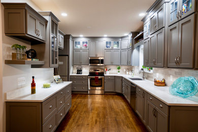 This is an example of a mid-sized arts and crafts galley eat-in kitchen in Cincinnati with an undermount sink, shaker cabinets, grey cabinets, quartz benchtops, beige splashback, ceramic splashback, stainless steel appliances, dark hardwood floors, brown floor and beige benchtop.