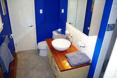 Minimalist white tile and subway tile bathroom photo in Philadelphia with a two-piece toilet, blue walls, a vessel sink and wood countertops