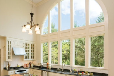 Example of a large transitional l-shaped open concept kitchen design in Cedar Rapids with a double-bowl sink, glass-front cabinets, white cabinets, solid surface countertops, stainless steel appliances and an island