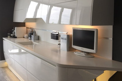This is an example of a large contemporary galley open plan kitchen in Hampshire with an integrated sink, flat-panel cabinets, white cabinets, solid surface benchtops, white splashback, black appliances, vinyl floors, with island and grey floor.