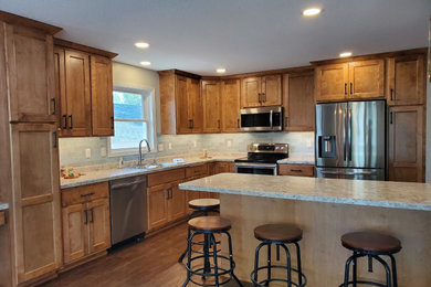 Large arts and crafts l-shaped laminate floor and brown floor eat-in kitchen photo in Other with a double-bowl sink, recessed-panel cabinets, medium tone wood cabinets, laminate countertops, green backsplash, glass tile backsplash, stainless steel appliances, an island and multicolored countertops